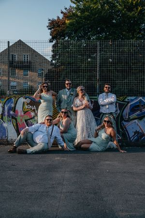 Wedding party relaxes along a graffiti wall in casual poses during an outdoor photo session.