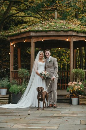 Wedding couple poses under a rustic wooden pergola with autumn foliage. The Venue, Halifax