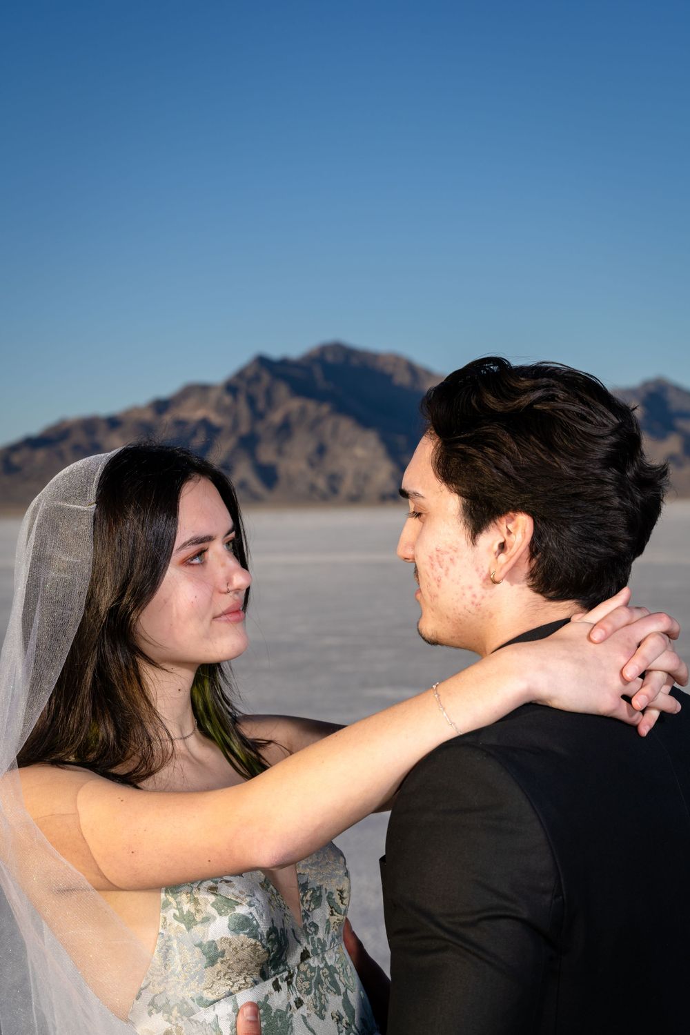 Romantic moment between couple on salt flats with mountains in background.