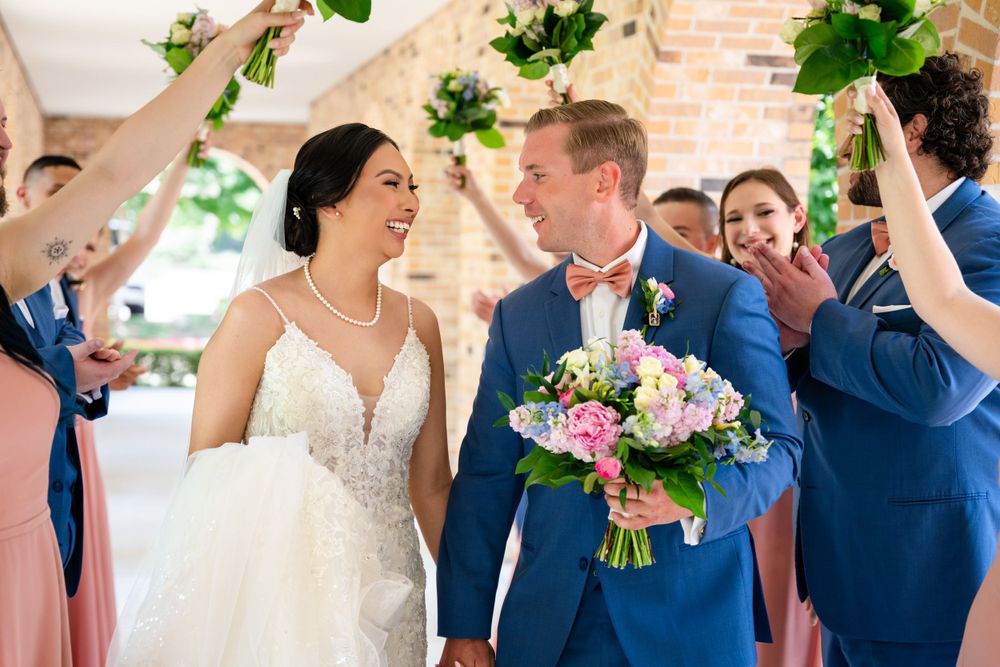 Wedding party celebrates with raised greenery branches in a brick-walled venue.