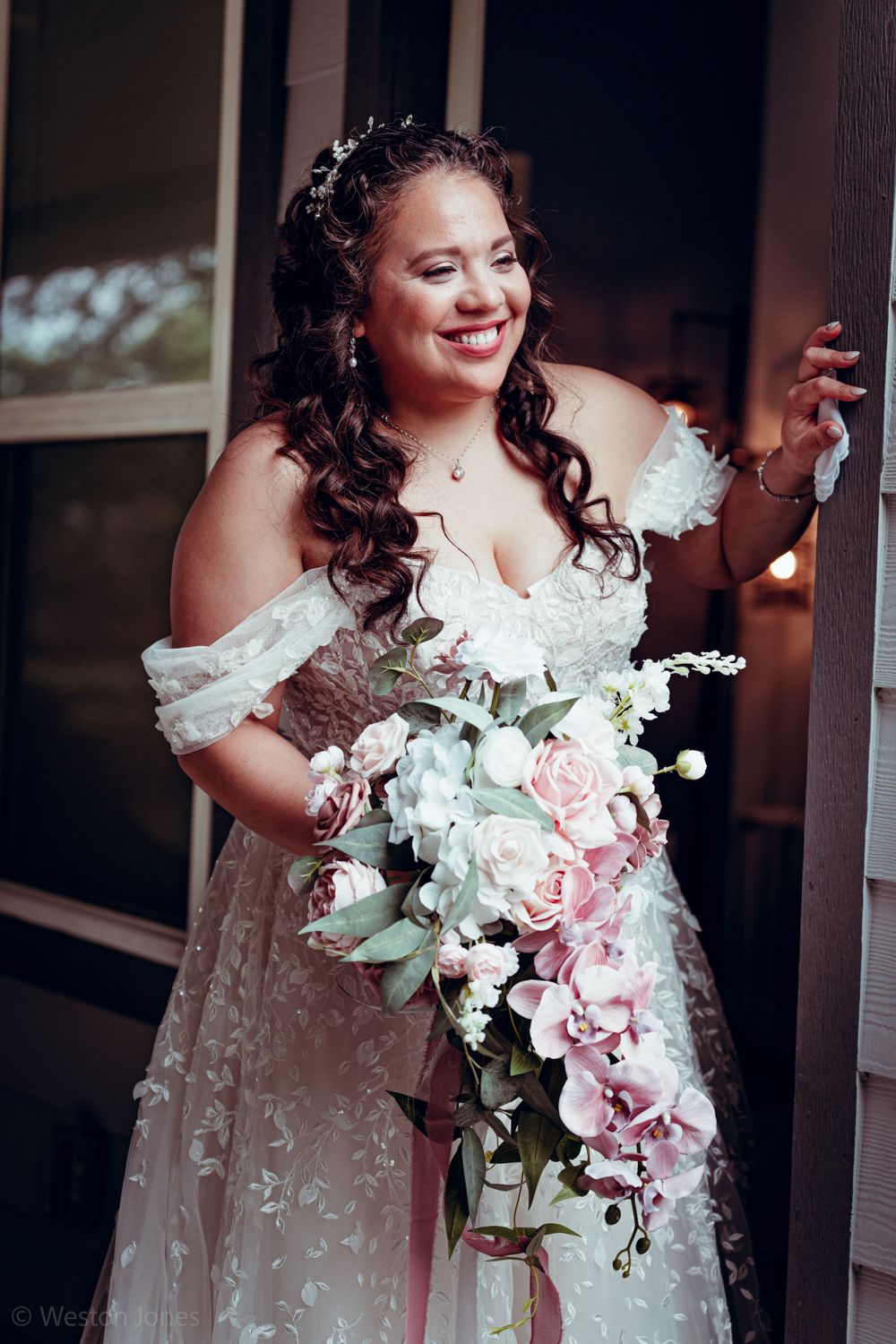 A person in a lace wedding gown holds a cascading bouquet of pink and white flowers.