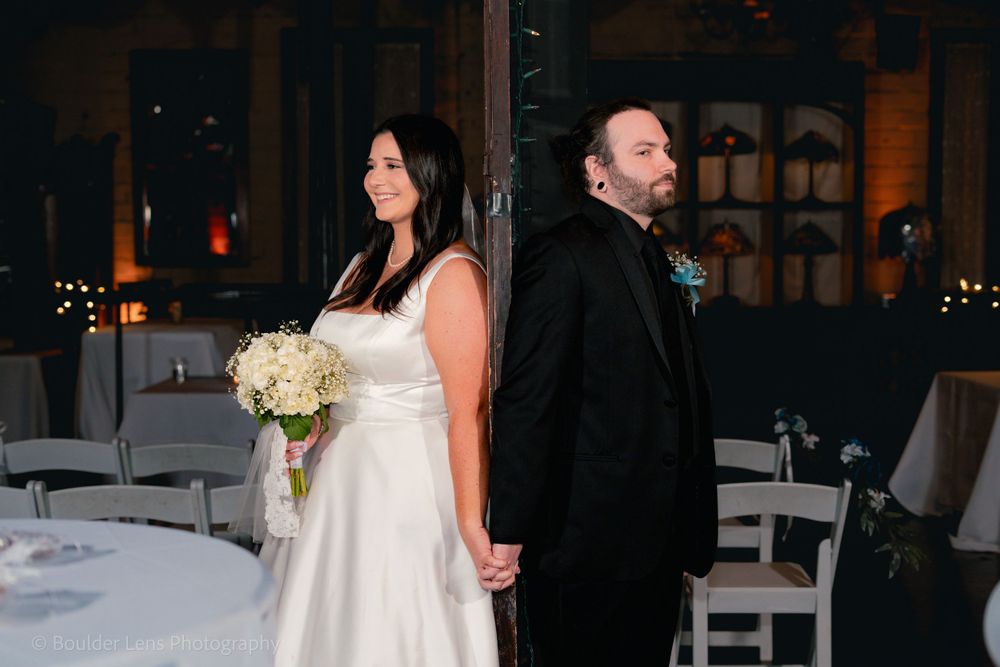 A couple in wedding attire stands back-to-back in an indoor reception venue.