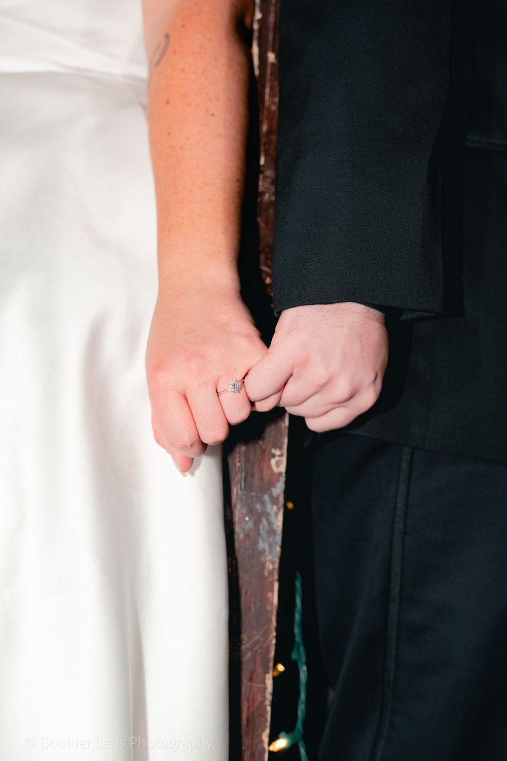 Close-up of two hands wearing wedding rings touching tenderly against a dark background.