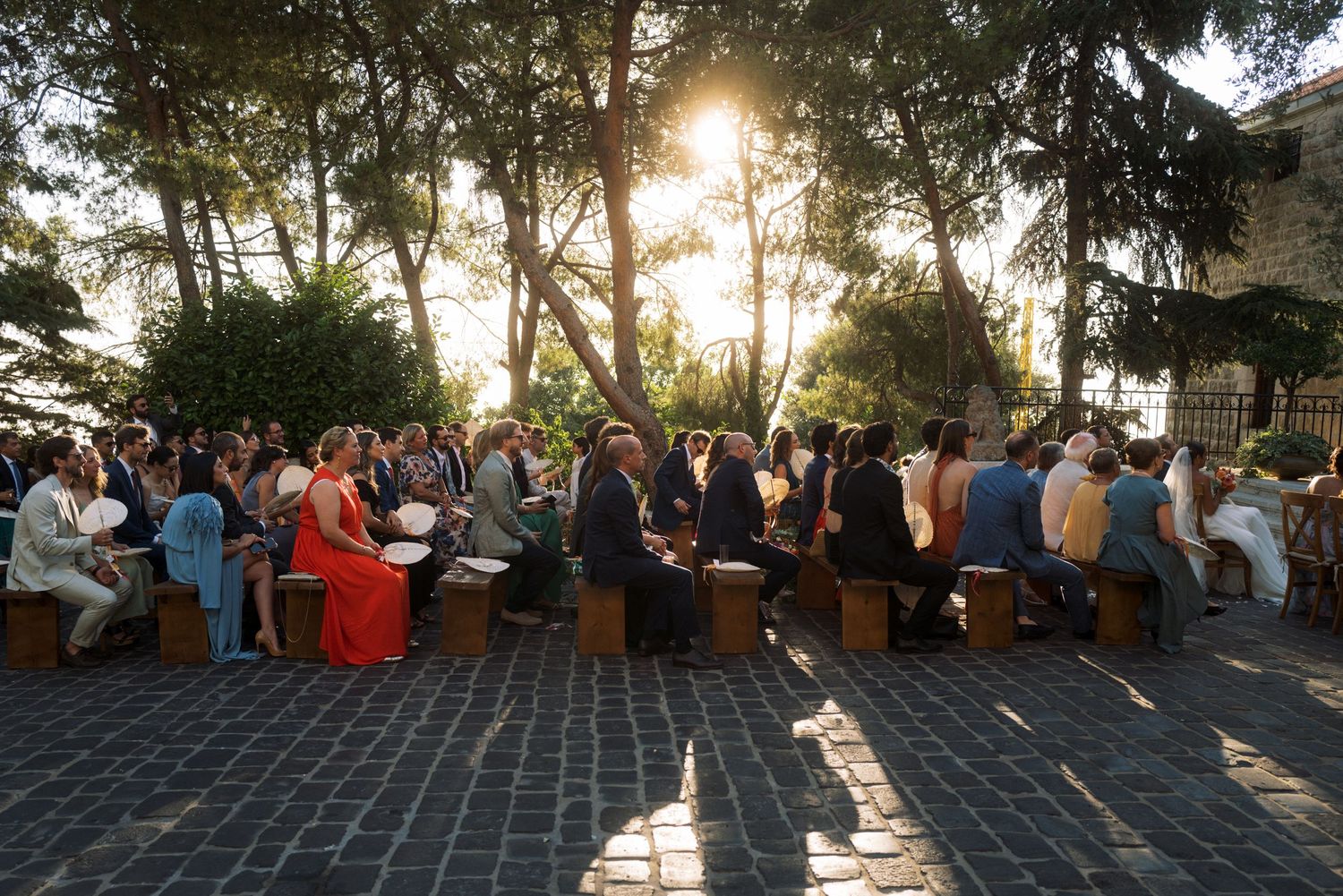 Wedding guests in white suits share laughter and drinks together at an outdoor celebration.