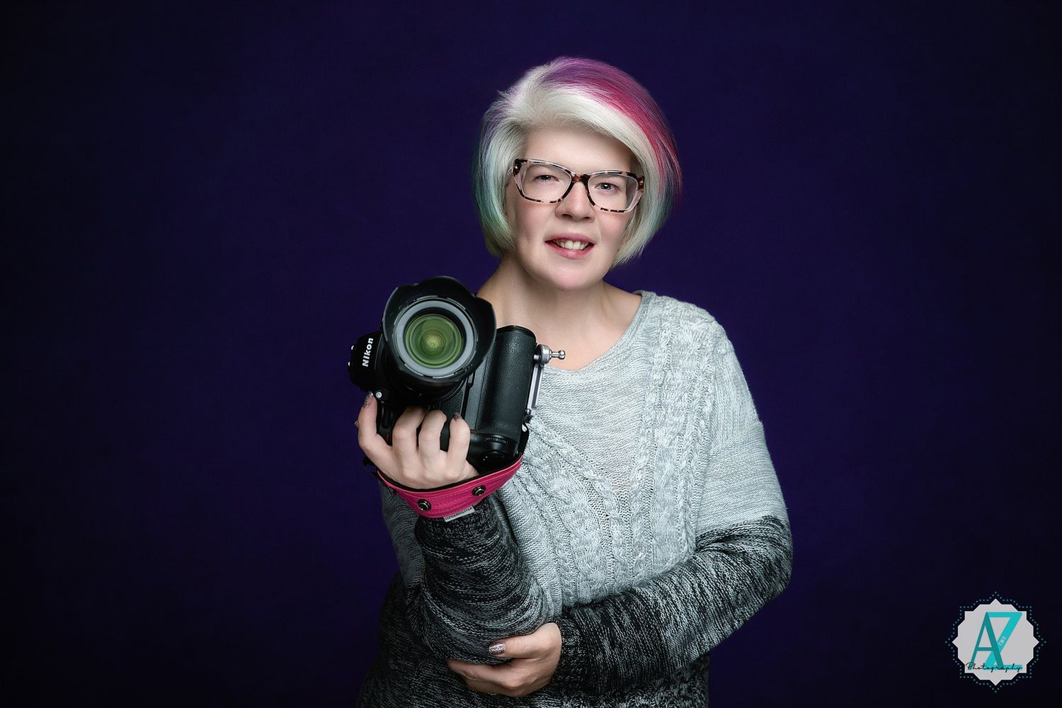 Portrait of photographer in orange sweater holding camera against dark background.