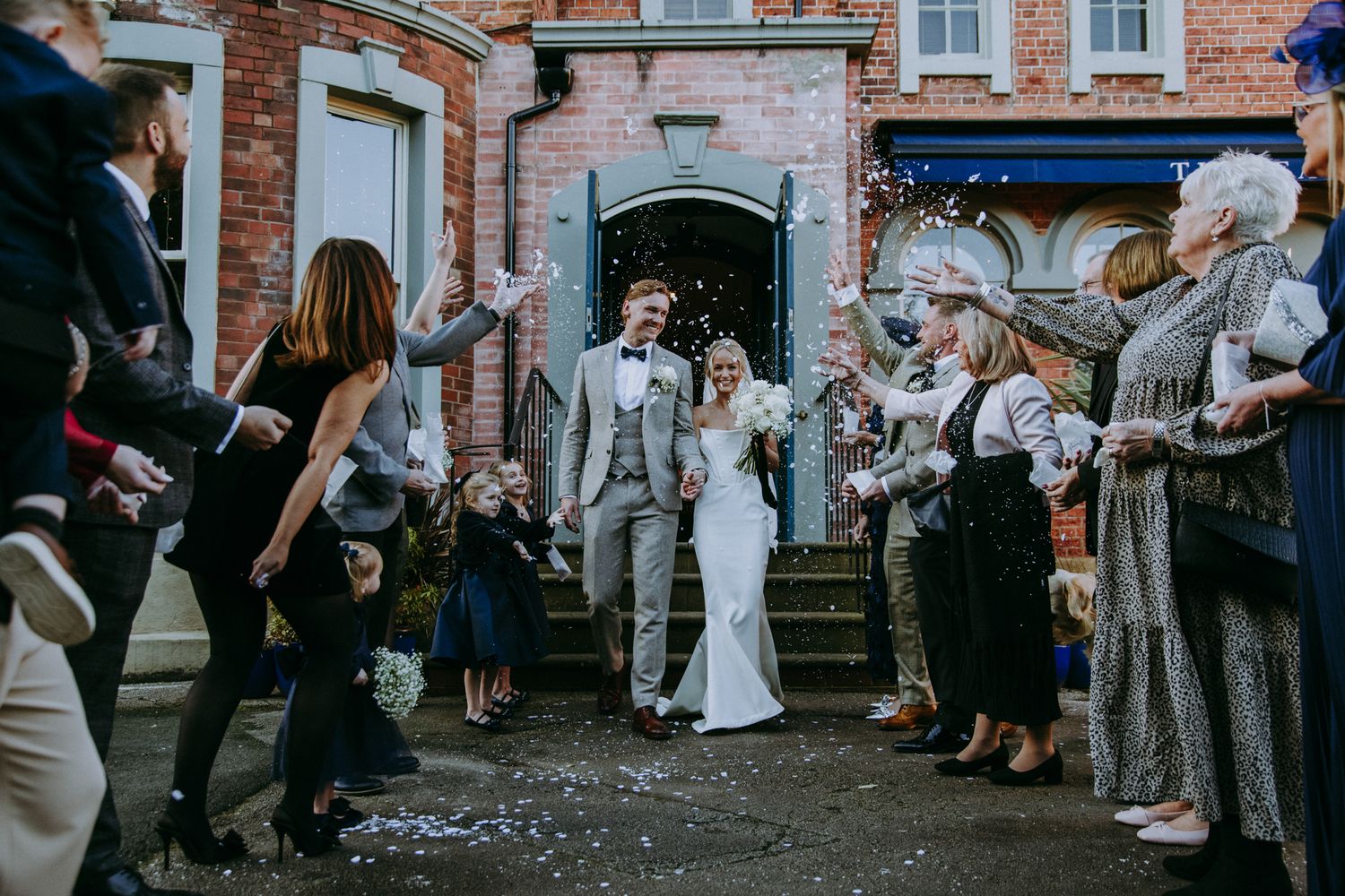 Wedding party exits historic brick building as guests throw confetti in celebration. Faversham, Leeds