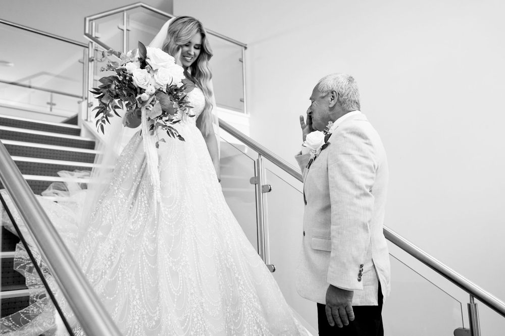 Black and white photo of emotional moment on stairs between bride and older man.