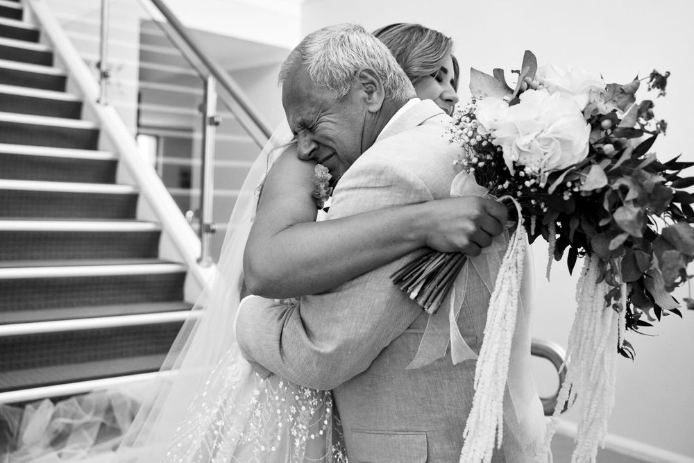 Black and white candid photo captures emotional embrace between bride and father.