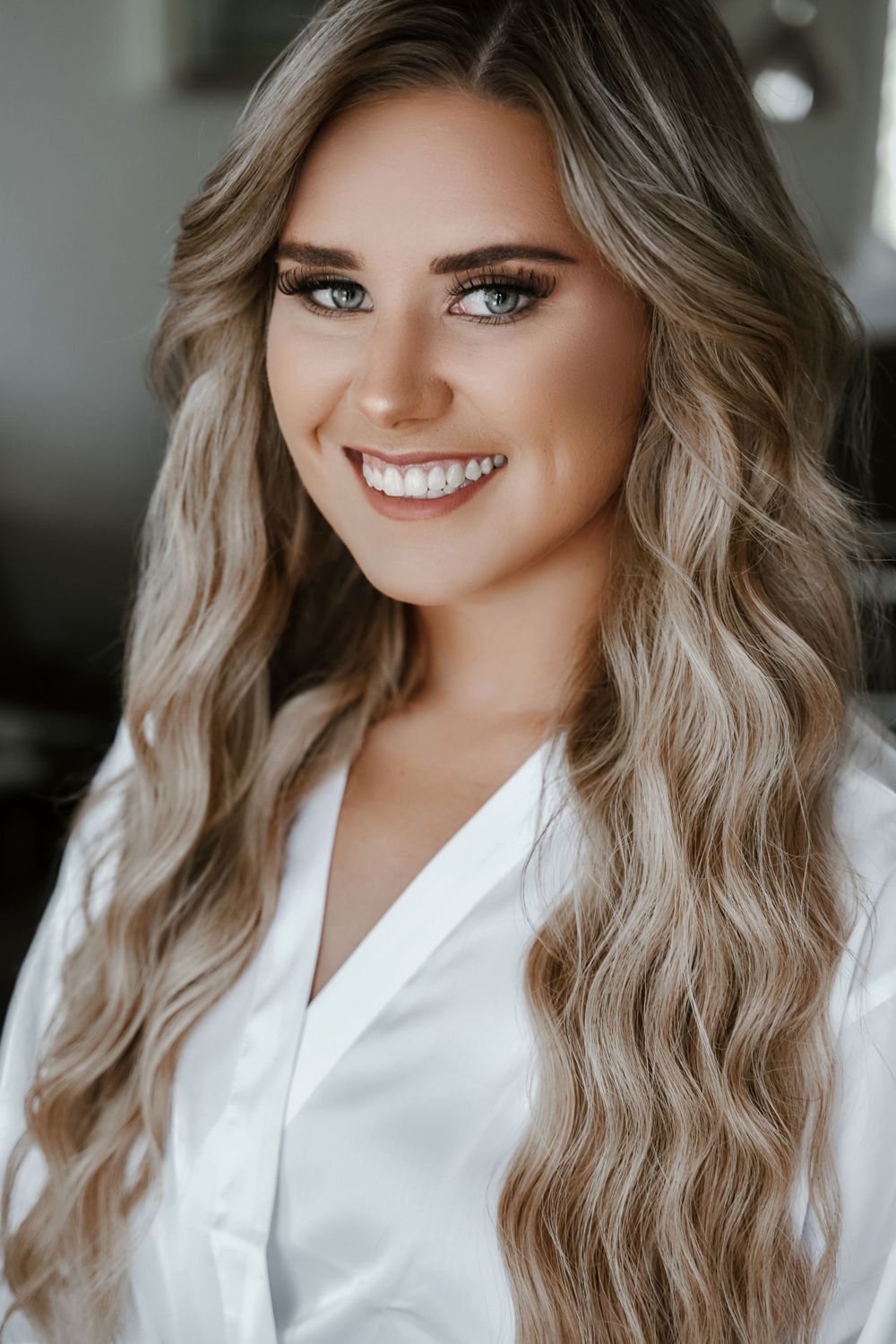 Close-up portrait of woman with wavy blonde hair and natural makeup wearing white top.