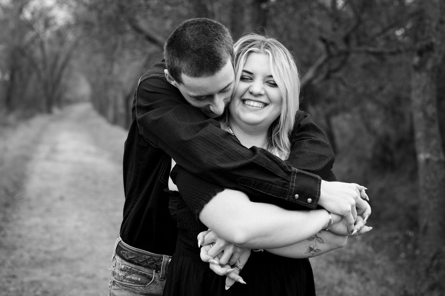 A couple embraces and shares intimate moments in a romantic outdoor photoshoot along a wooded path.