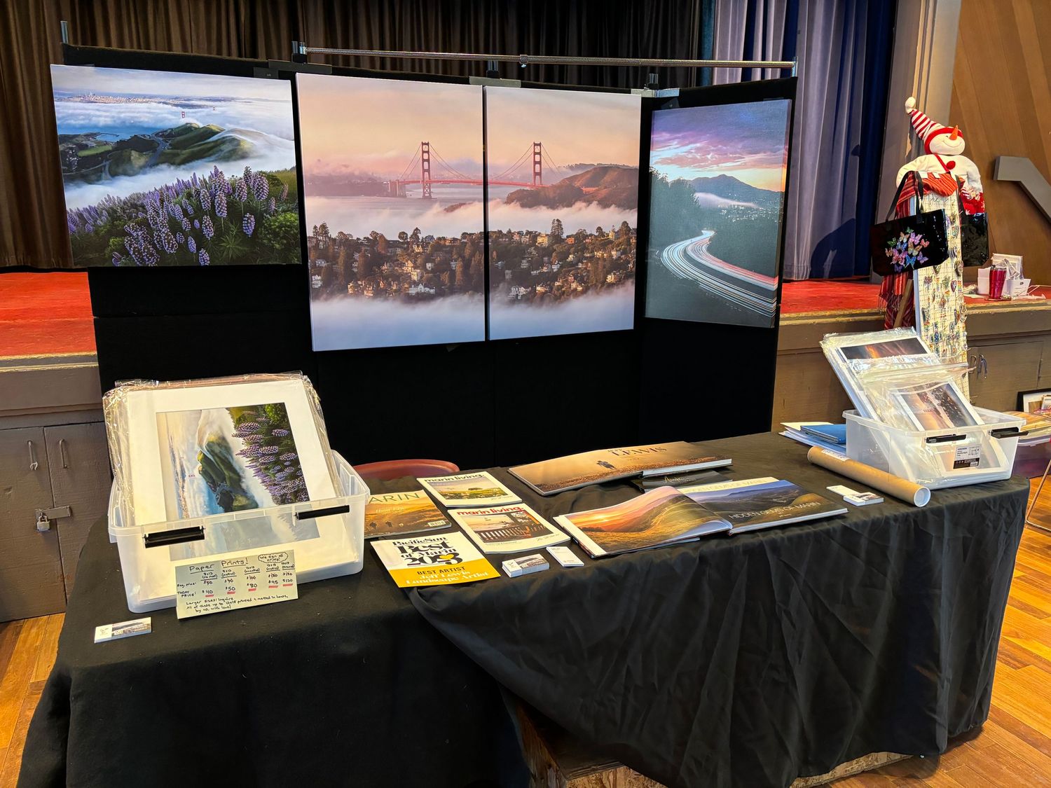 Photography display booth showing landscape prints of foggy San Francisco Bay scenes on multiple monitors.
