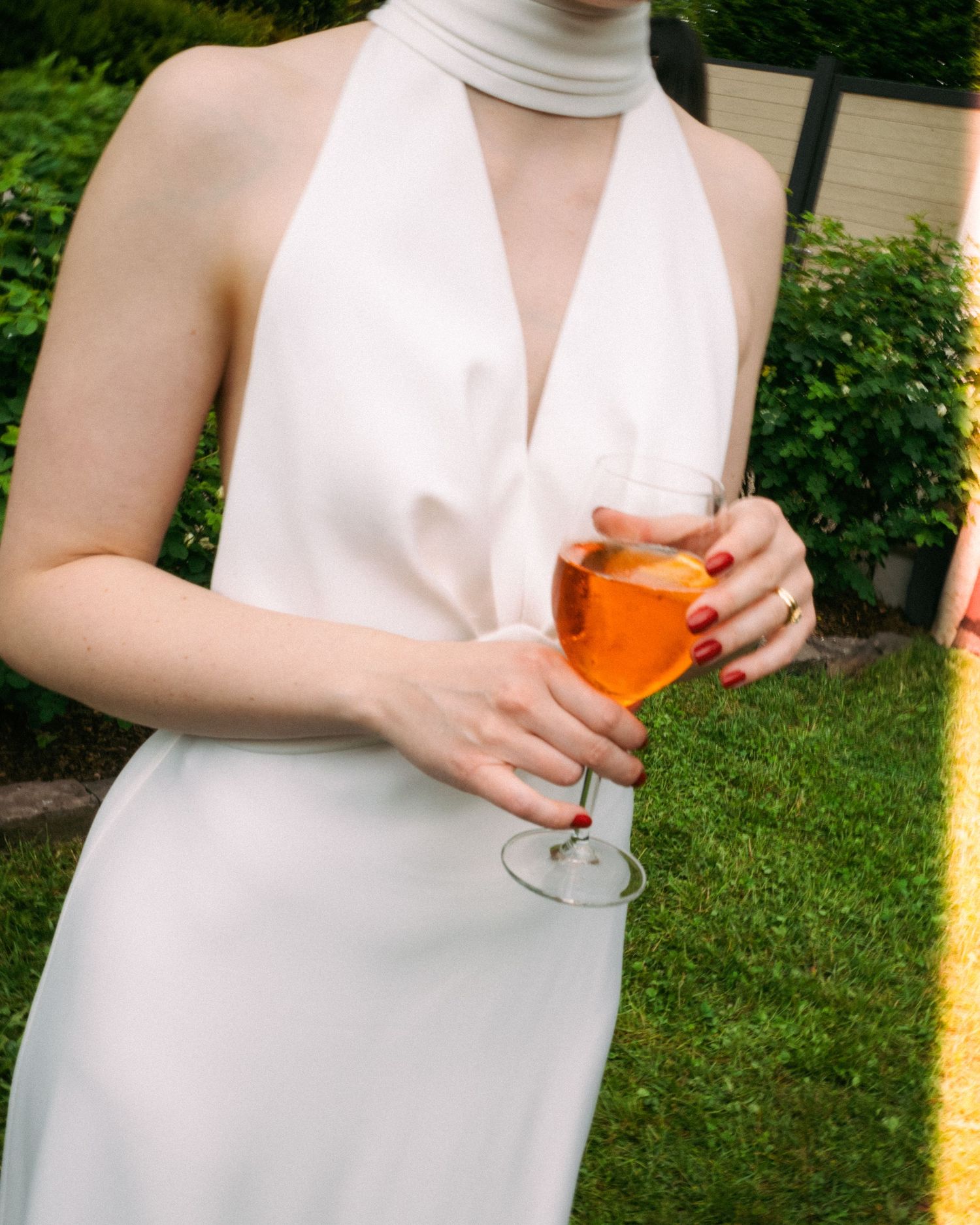 A close-up of someone holding an orange cocktail while wearing a white halter dress.