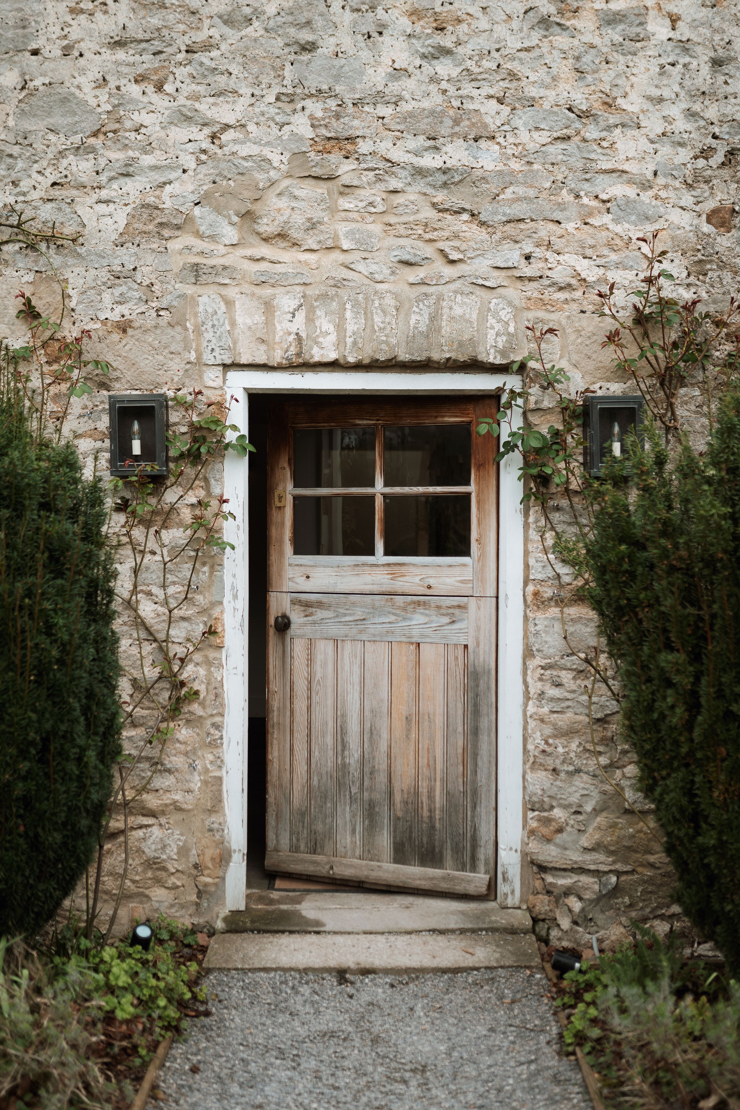 A weathered wooden door with lanterns set in an old stone wall surrounded by greenery at the farmhouse, Middleton lodge