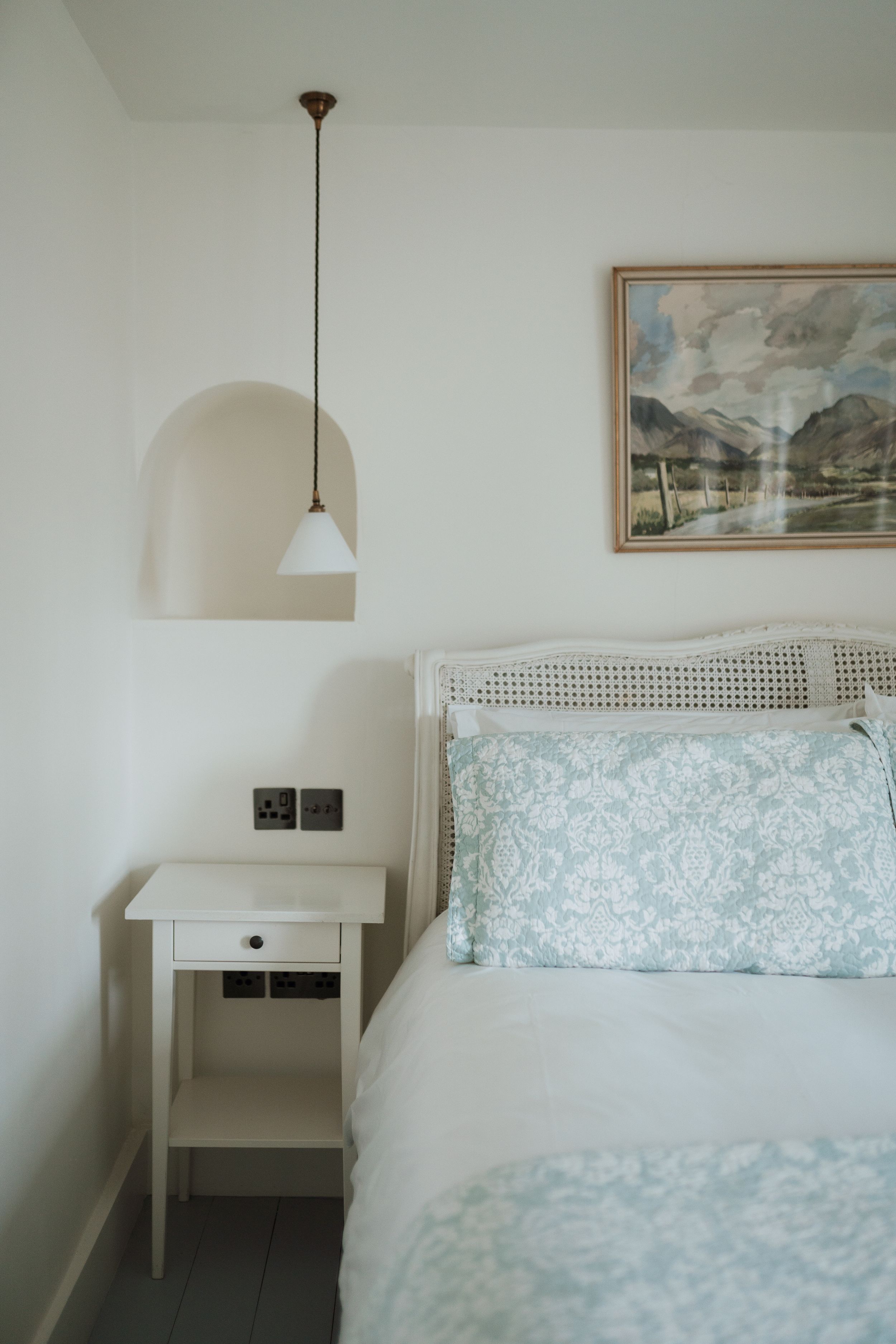 A serene bedroom with white bedding, pendant light, and landscape artwork in soft neutral tones at Middleton lodge