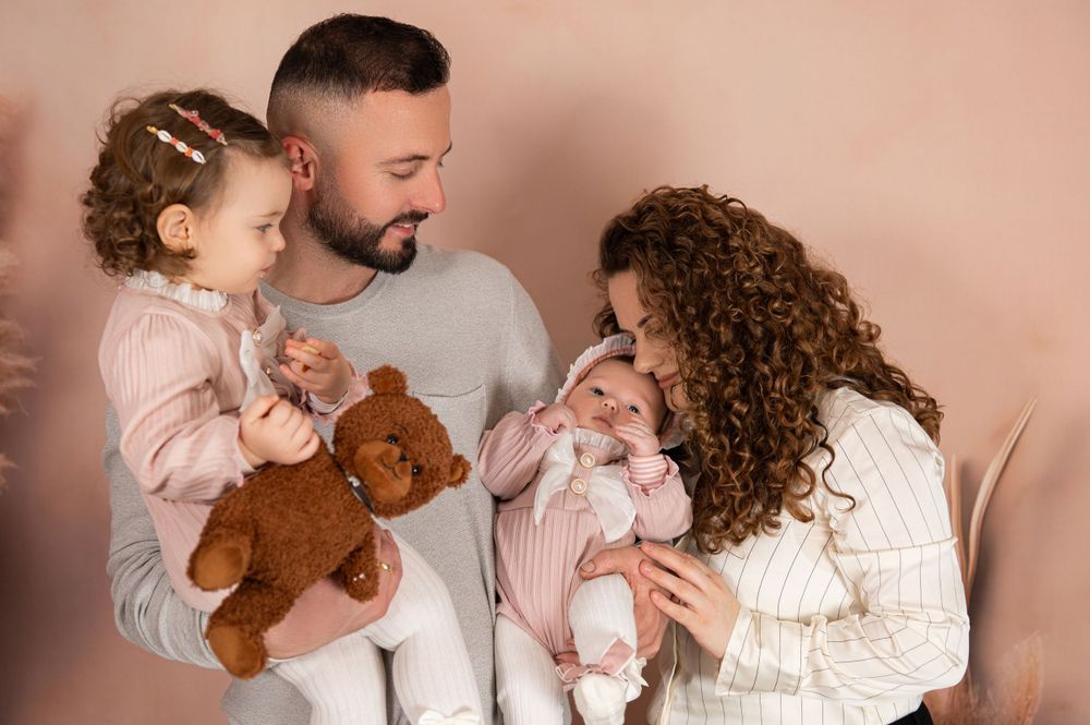 Intimate family moment with teddy bear against neutral backdrop with pampas grass.