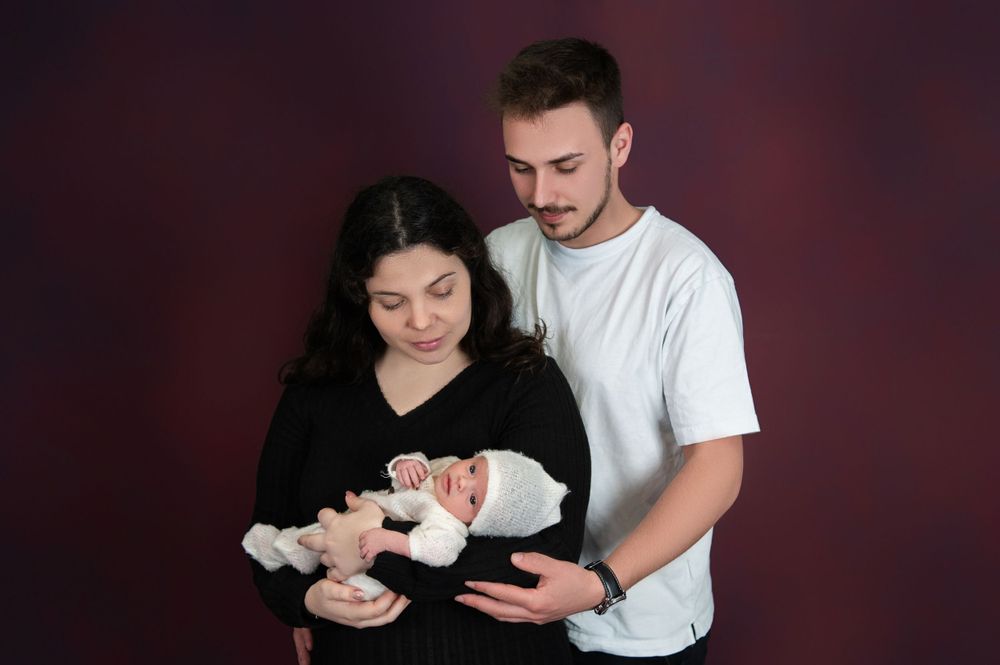 Studio portrait with newborn baby against dark burgundy background.