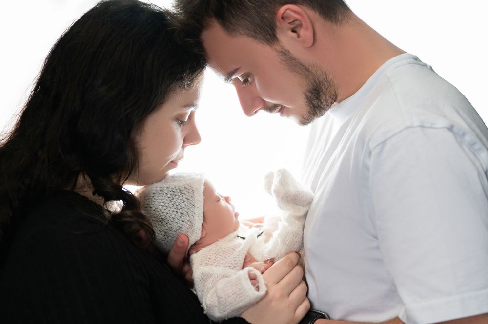 Intimate family moment with newborn baby against bright background.