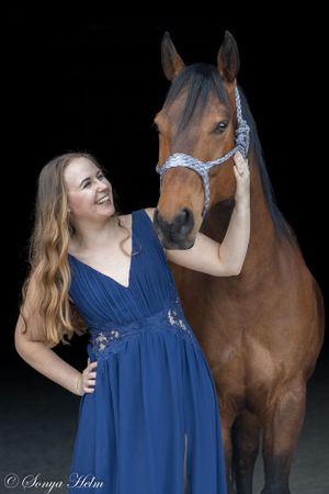 Person in navy gown poses with bay horse wearing light blue halter against black background.