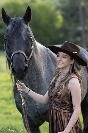 Grey horse and person in brown dress and cowboy hat pose in outdoor setting.