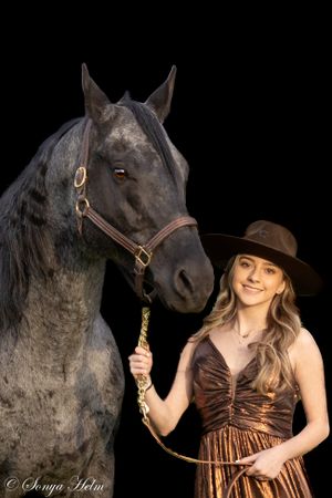 Black horse poses with person in brown dress and western hat against dark background.