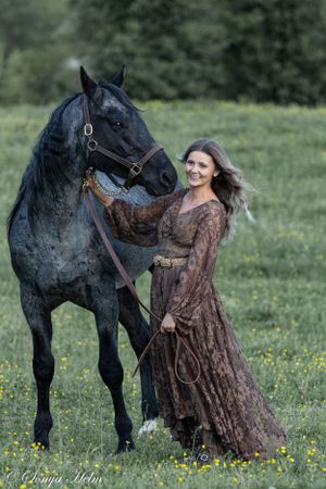 A beautiful black horse stands in a wildflower meadow with someone in a vintage brown lace gown.