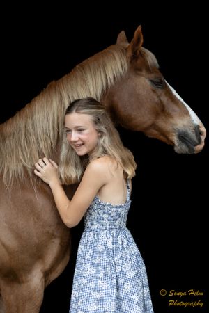 A beautiful chestnut horse poses with someone in a blue and white summer dress.