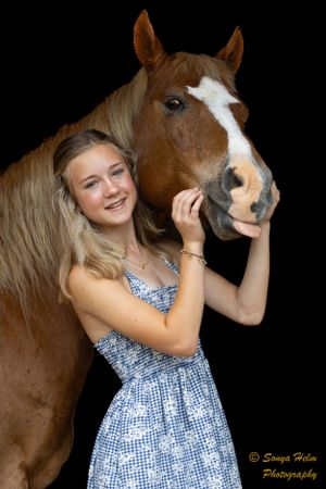 A person in a blue dress stands with a brown horse with white markings against a black background.