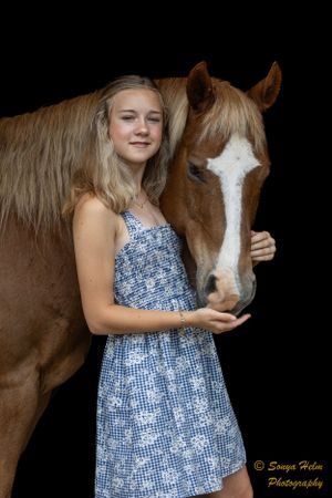A person in a blue floral dress poses with a brown horse with a white face marking.