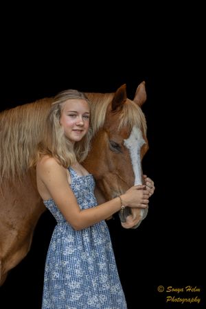 Brown horse with white blaze poses against black background with companion wearing blue floral dress.