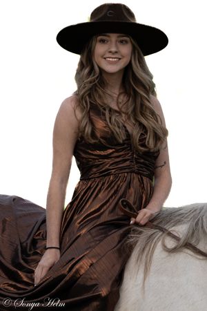 Stylish bronze dress and wide-brimmed hat ensemble shown while horseback riding.