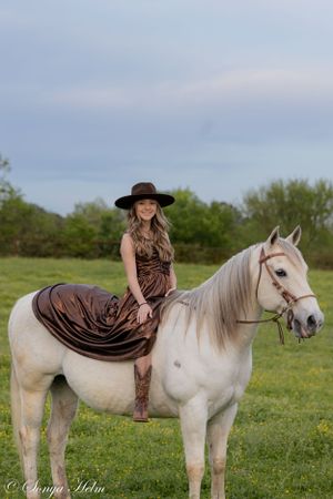 Beautiful white horse with flowing mane stands in green field wearing western riding gear.