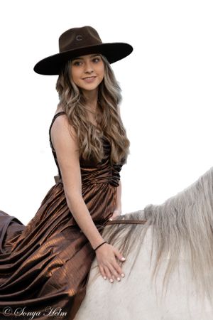 Western style portrait featuring brown dress and hat paired with white horse.