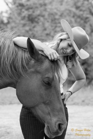 Black and white photo of person in cowboy hat sharing tender moment with horse.