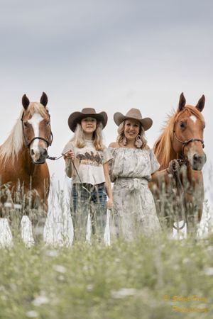 Four horses and their handlers stand in a field of tall grass and wildflowers.