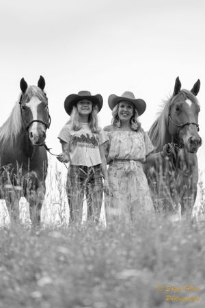 Black and white portrait of horses and handlers standing in a wildflower meadow.