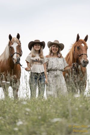 Two horses and their handlers pose together in a meadow of white wildflowers.
