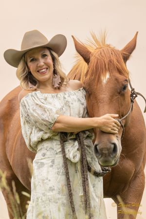 Beautiful chestnut horse with white blaze poses with companion in western attire.