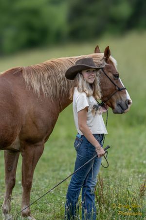 Chestnut horse and companion in western wear stand in green summer field.