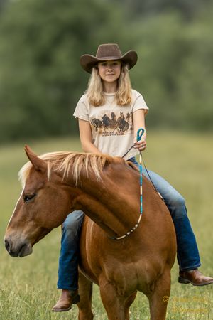 Chestnut horse being ridden bareback through a green field on a summer day.