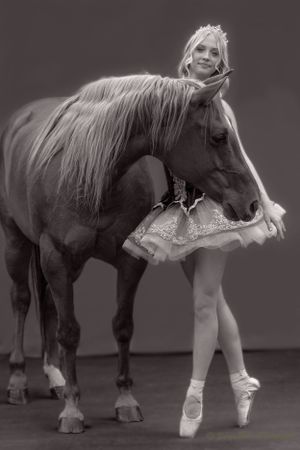 A ballerina in a tutu poses en pointe next to a dark horse in a dramatic black and white photo.