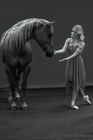 A monochrome portrait of a dancer in a flowing dress connecting with a majestic horse.