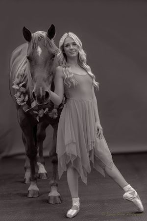 An elegant black and white portrait of a dancer in pointe shoes posing with a decorated horse.