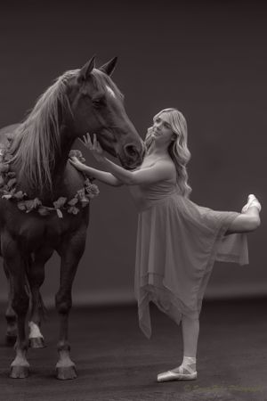 A black and white portrait capturing intimate connection between dancer and horse in studio setting.
