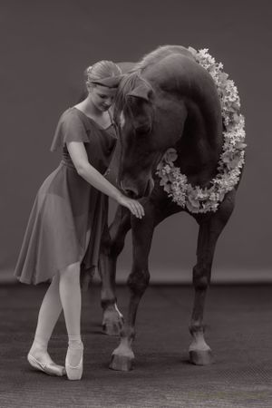 Monochrome photo of graceful ballet pose with decorated horse.