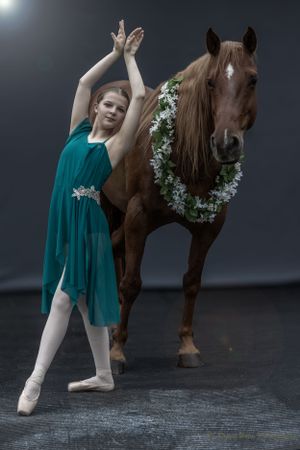Ethereal dance pose with horse wearing flower garland under dramatic lighting.