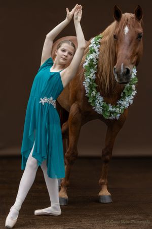Dancer in flowing teal dress performs alongside decorated horse.