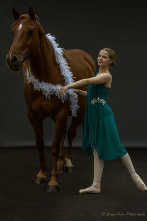 Ballet photographer captures dancer arranging white garland on brown horse in studio setting.