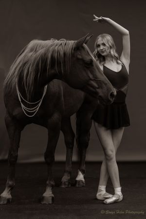 A monochrome portrait of a dancer in ballet attire posing elegantly with a horse.