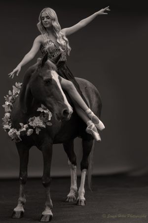 A dancer strikes an expressive pose while seated on a horse adorned with flowers.