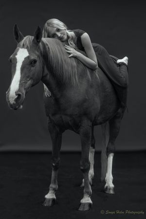 A black and white portrait showing a relaxed pose on horseback in artistic lighting.